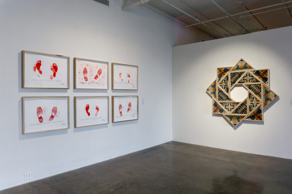 Wall on the left holds six framed works on paper, featuring red footprints on each. Spiral, design on the right made using Pendleton beach towels and triangular frames.