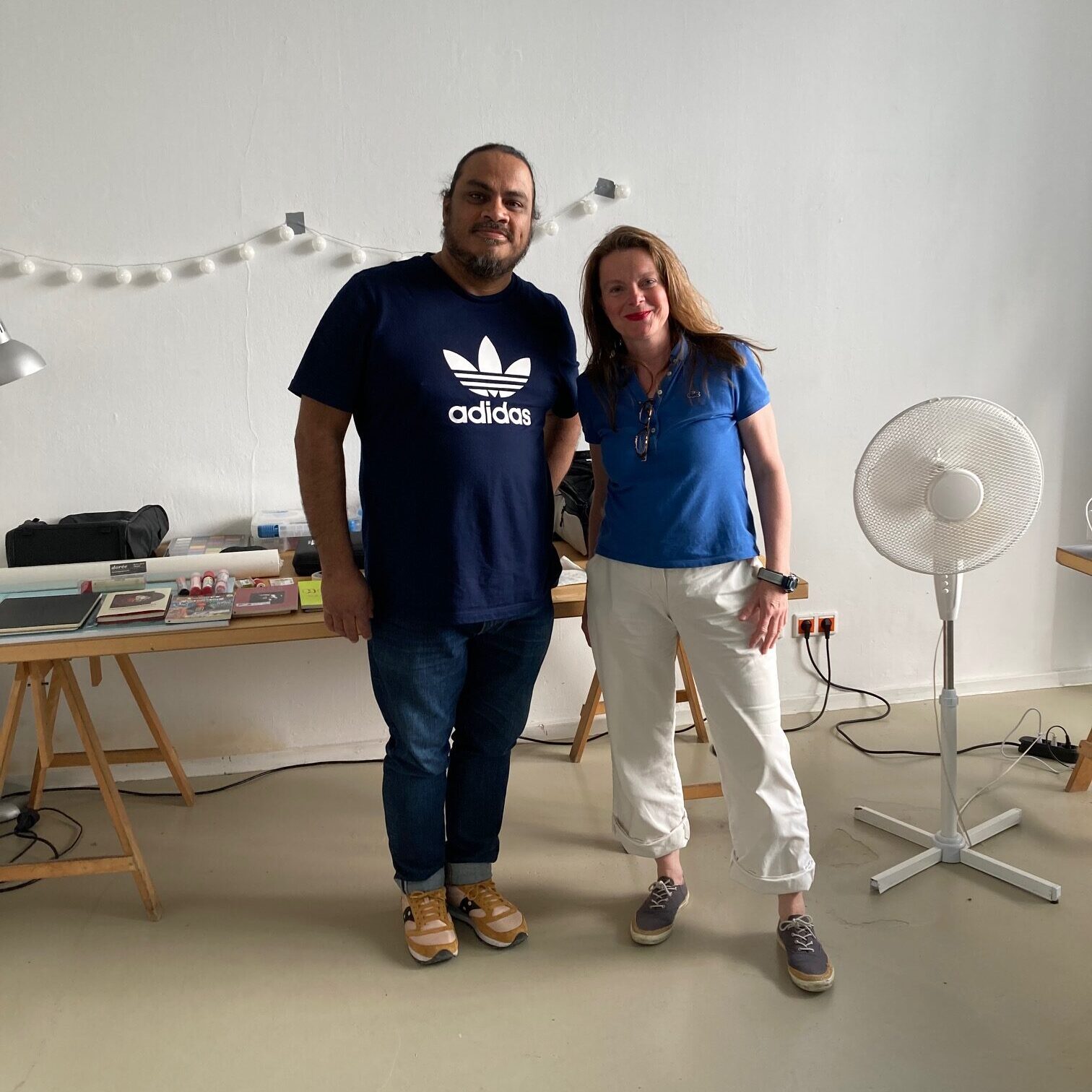 A man and a woman standing side by side in front of a table of art supplies.