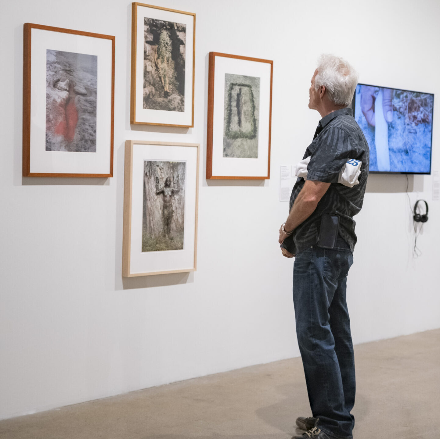 Man looking at wall of four framed photographs. The photographs include scenes of nature, with a female figure or impression of the figure.