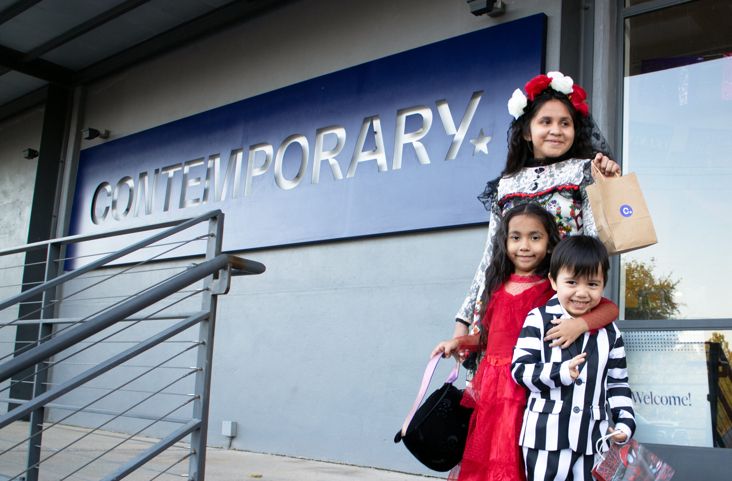 Three kids in halloween costumes in front of Contemporary sign