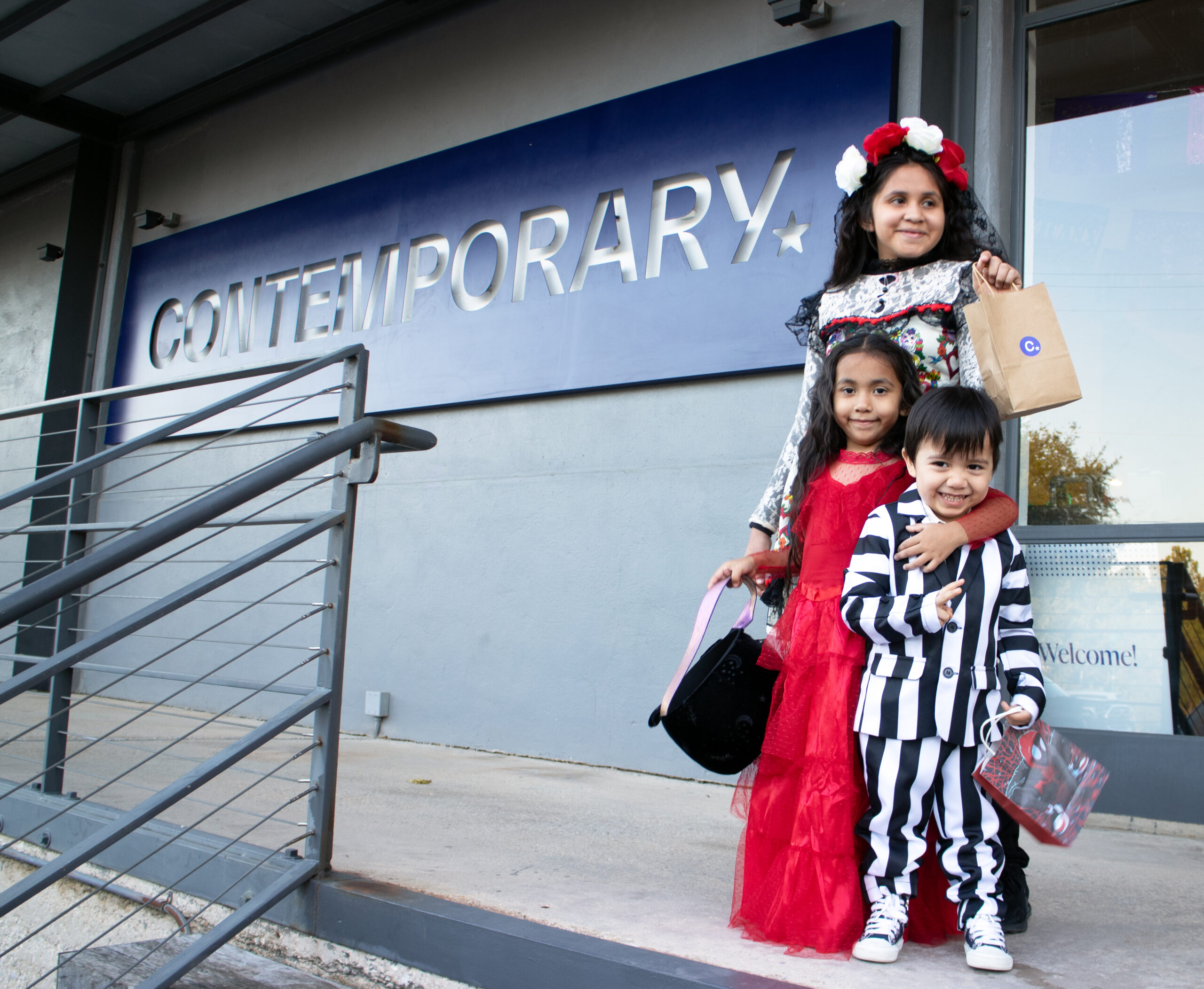 Three kids in halloween costumes in front of Contemporary sign